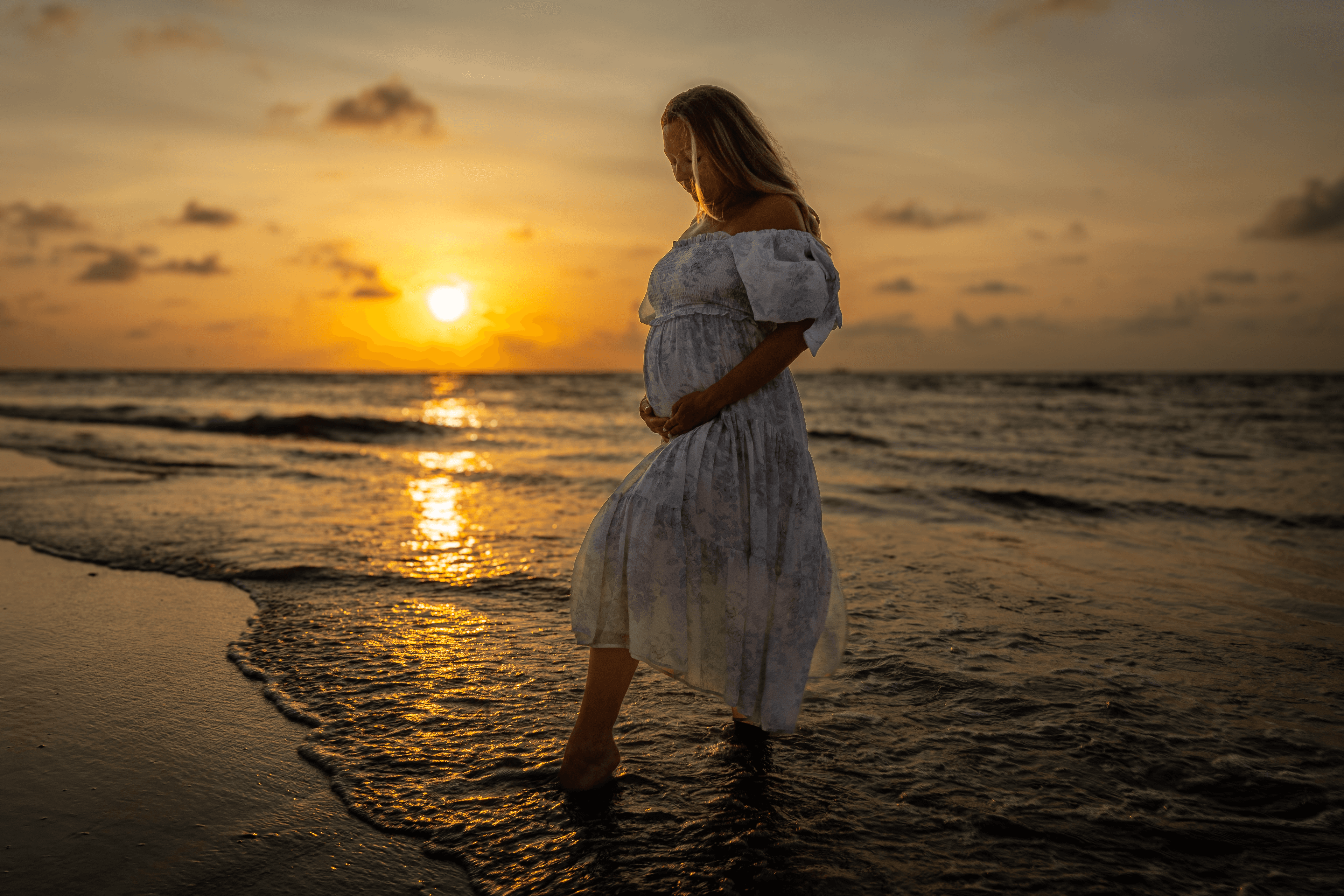 Expecting parents embracing at sunset